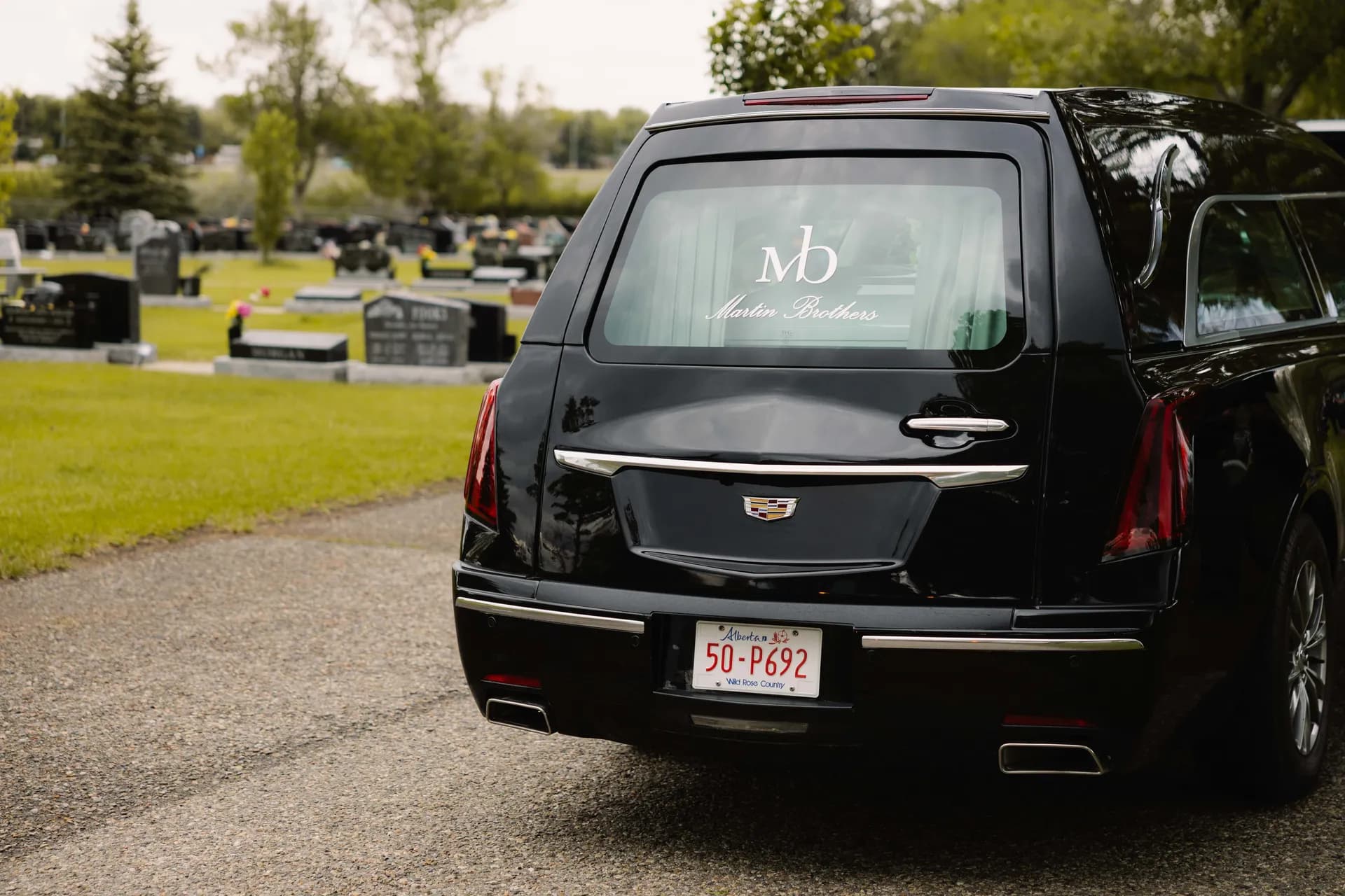 A black Martin Brothers Cadillac hearse parked respectfully at a cemetery - providing compassionate funeral services in Lethbridge since 1907