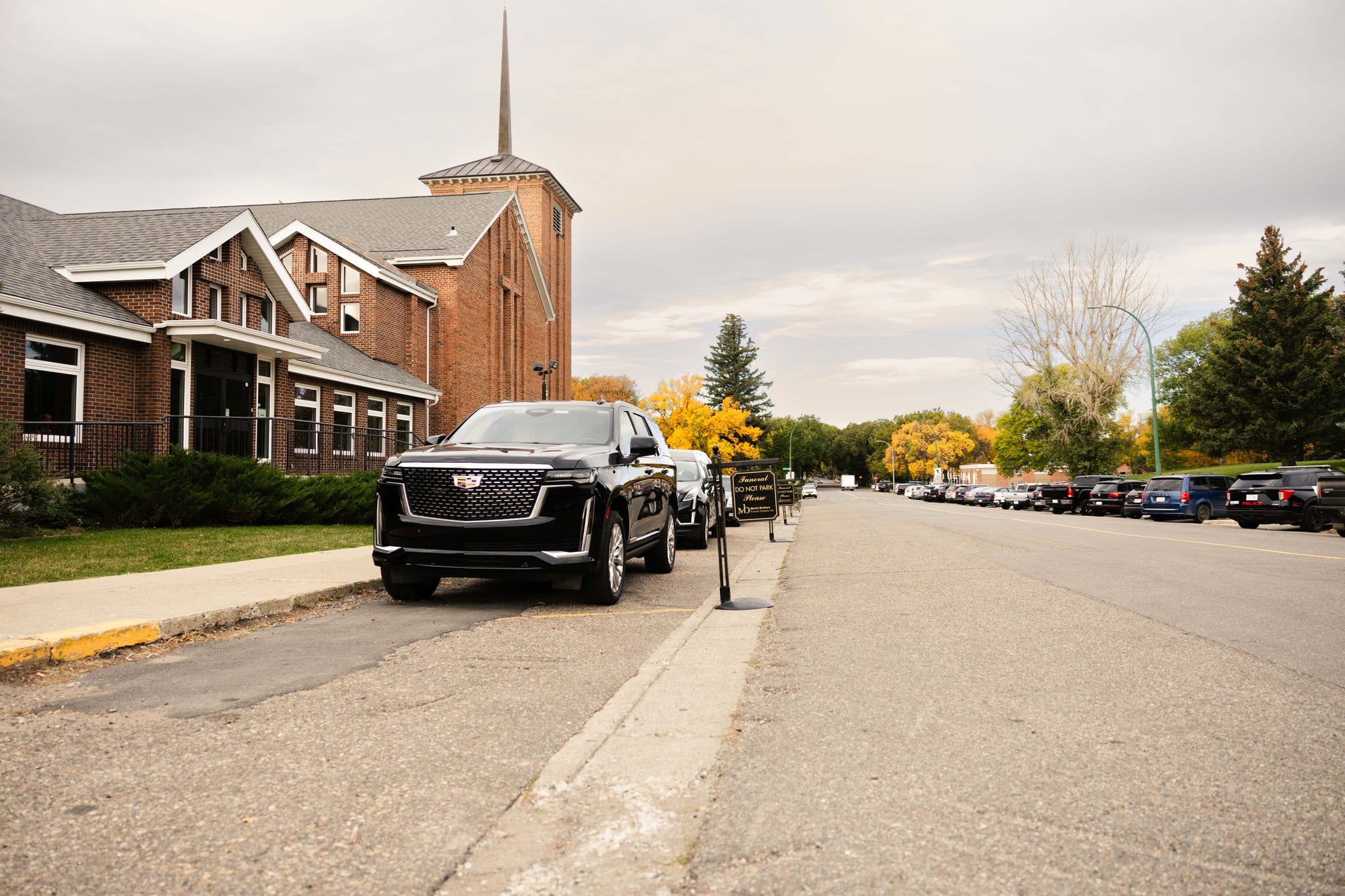 Black Cadillac Escalade lead vehicle waiting outside a Lethbridge church in autumn