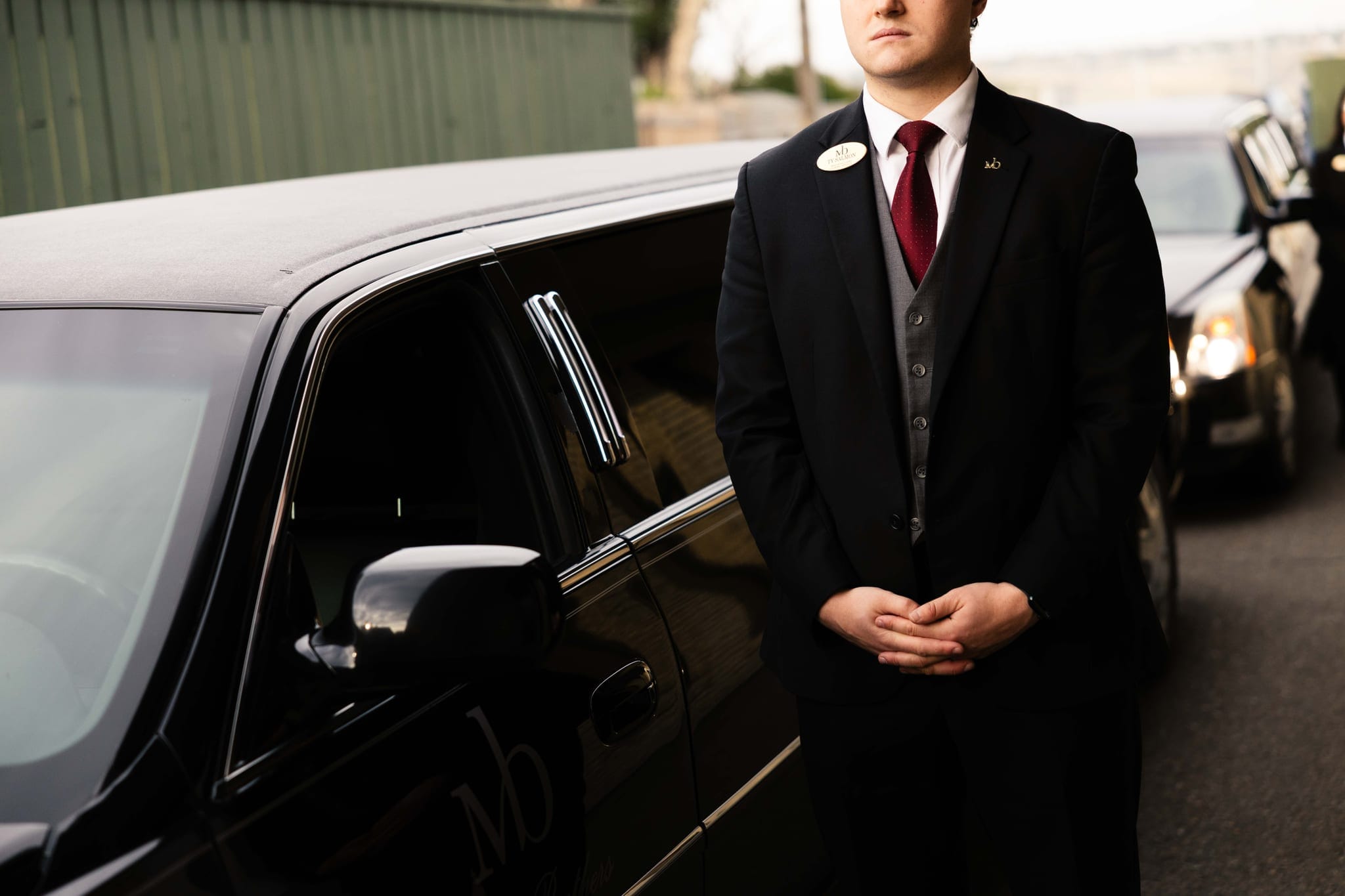 A Martin Brothers director standing quietly beside a black Cadillac family limousine