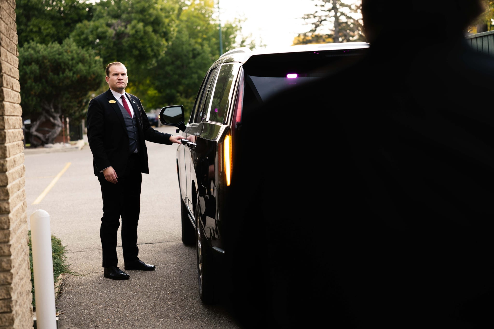 A Martin Brothers director holding open the door of a black Cadillac for a family