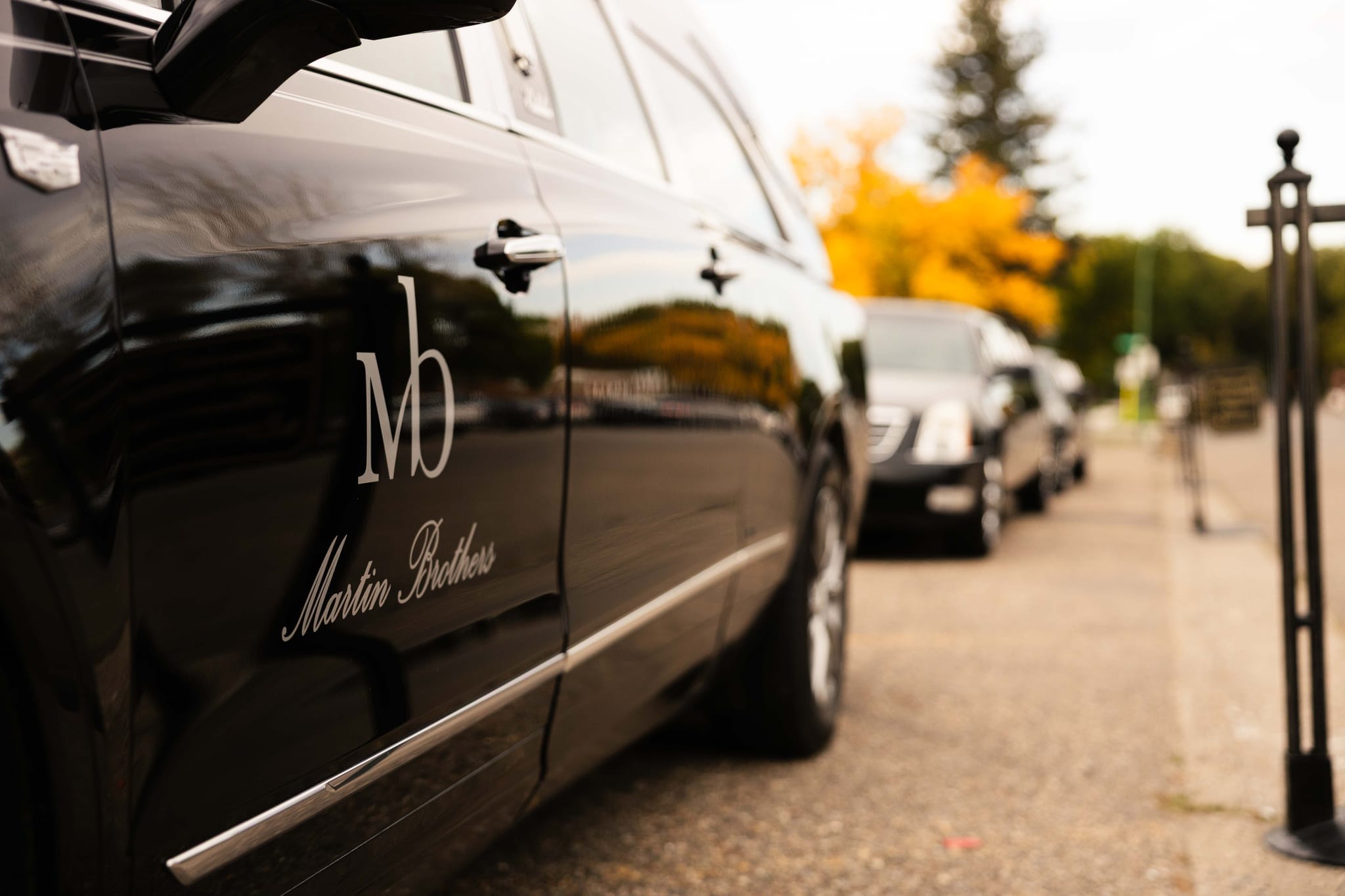 The Martin Brothers monogram on the side of a black Cadillac funeral coach, a procession waiting behind