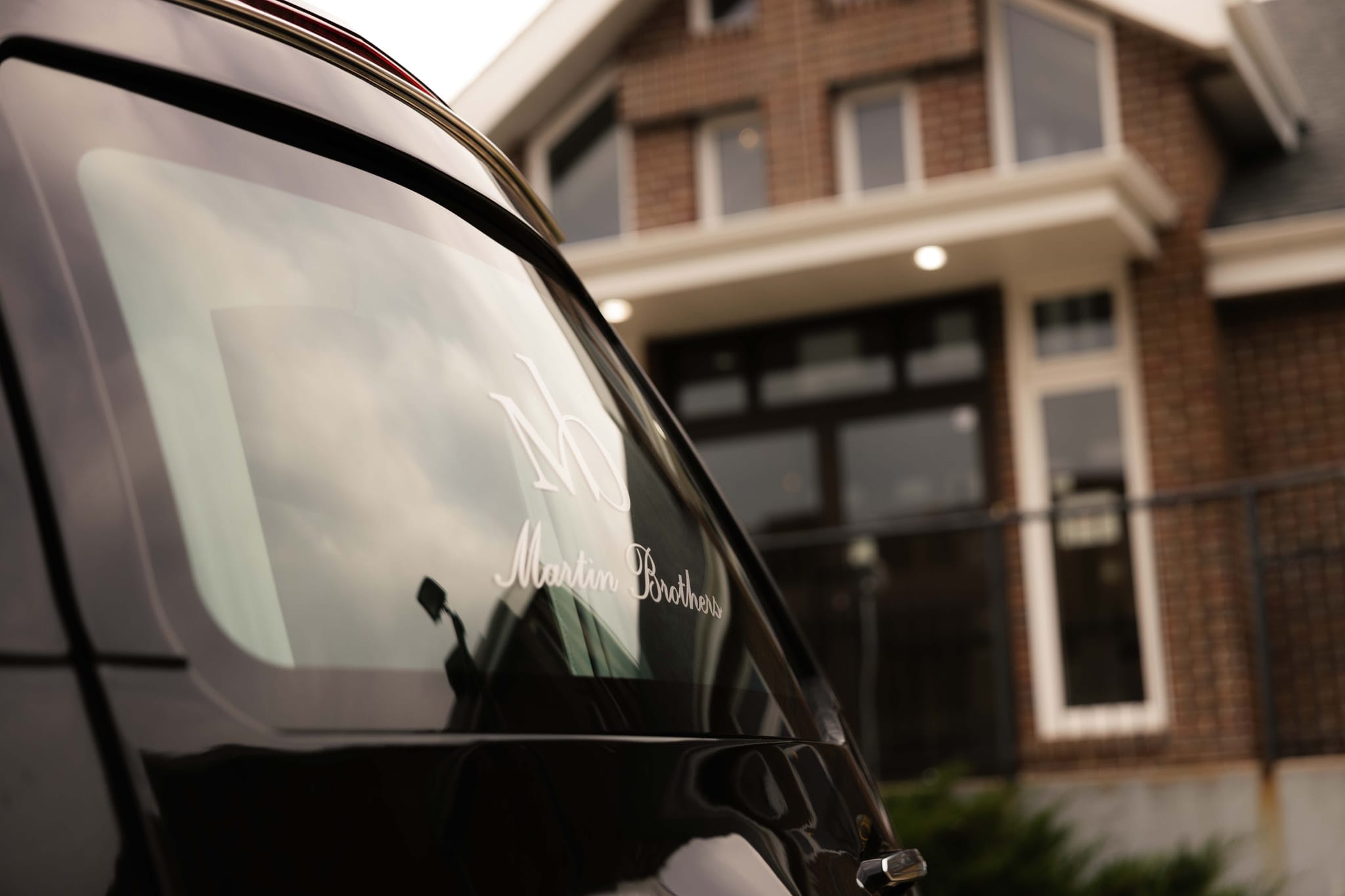 The Martin Brothers monogram etched on the windshield of a funeral coach, reflecting the autumn street