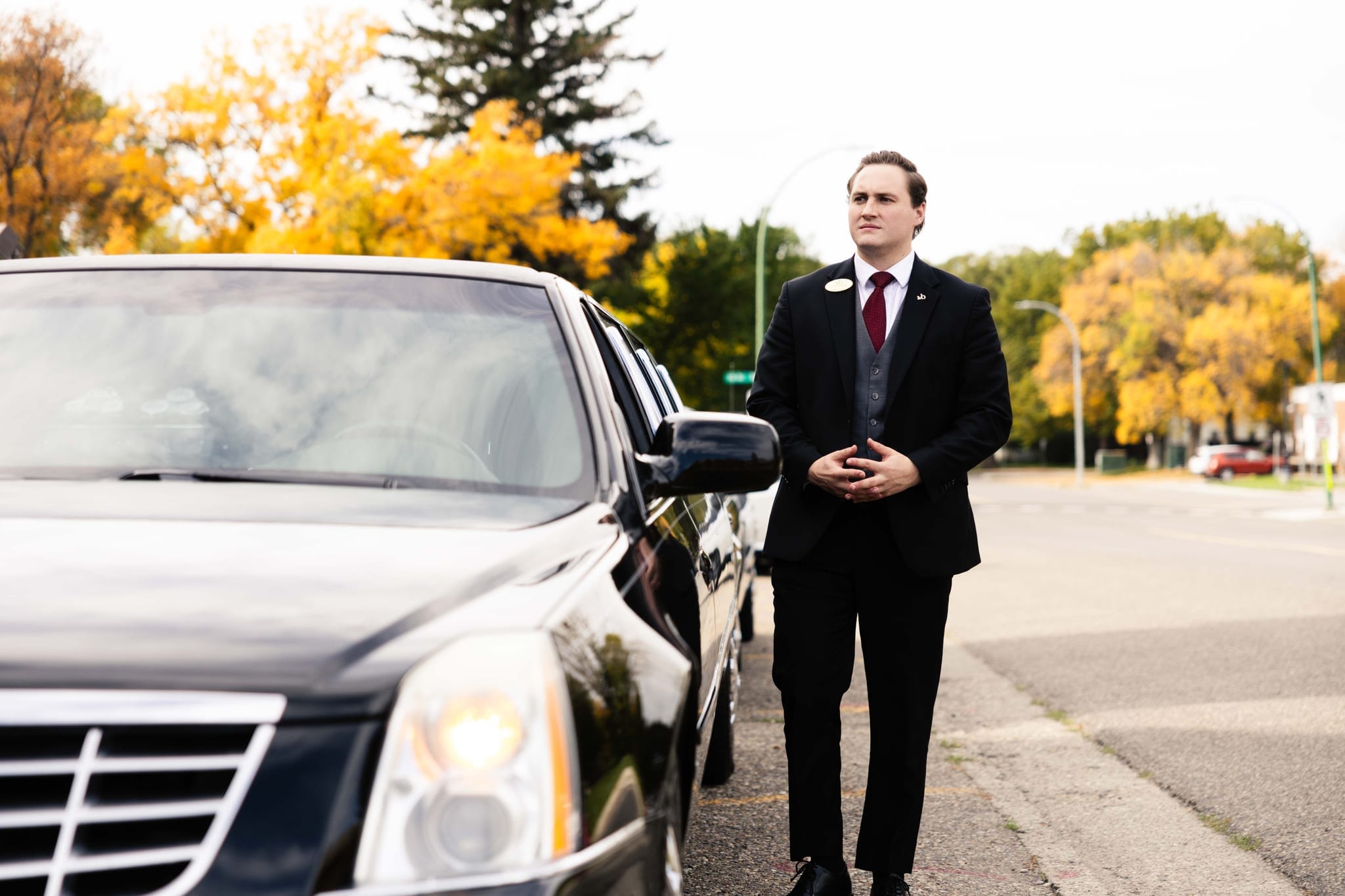 A Martin Brothers director standing beside a black Cadillac on a tree-lined autumn street