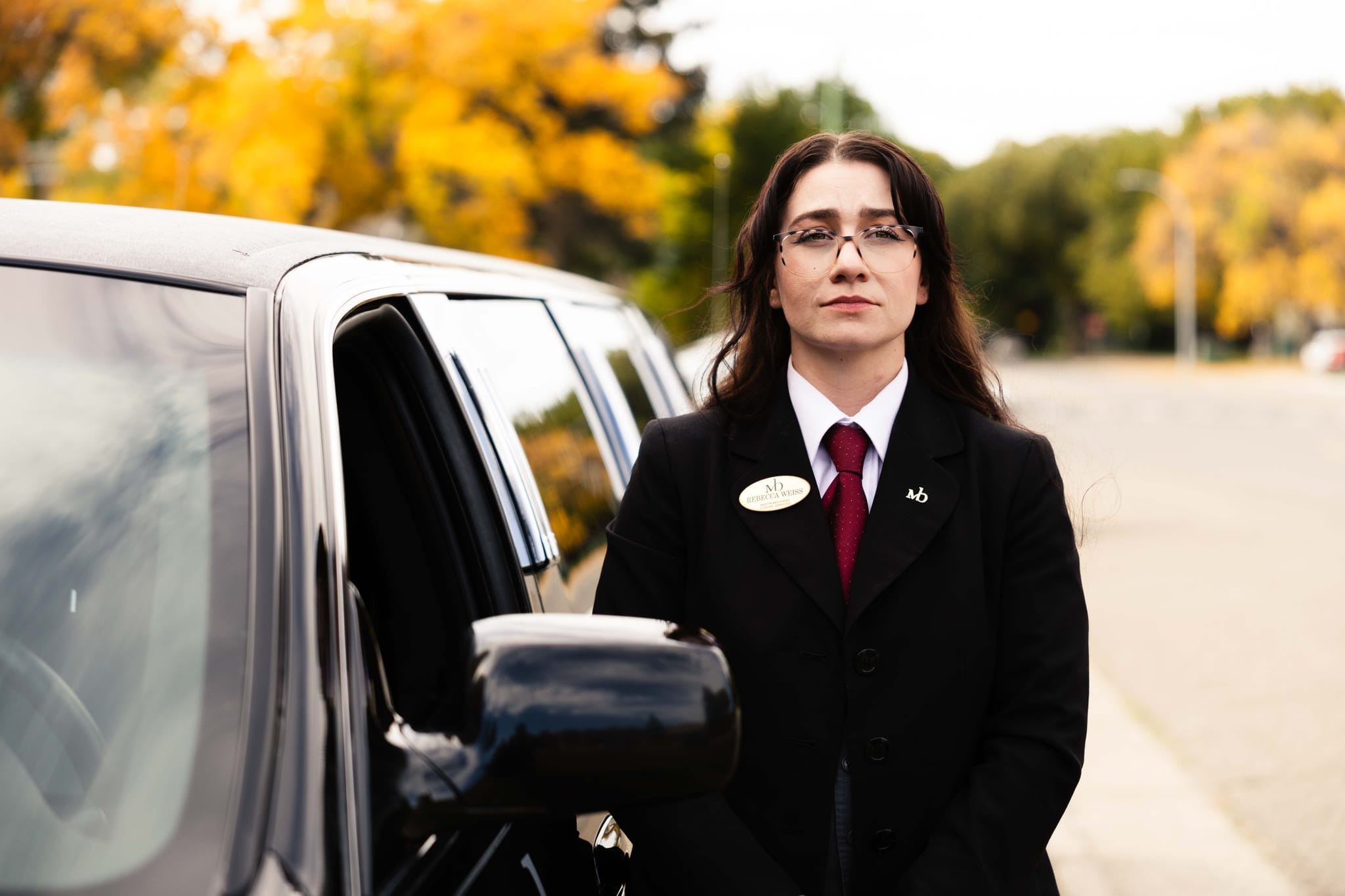 A Martin Brothers director standing beside a black Cadillac stretch limousine on an autumn street
