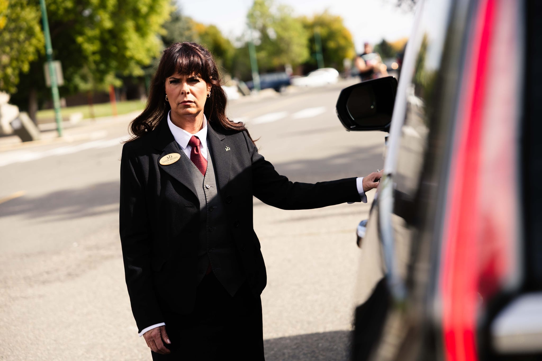 A Martin Brothers director standing at the door of a black Cadillac on a quiet street