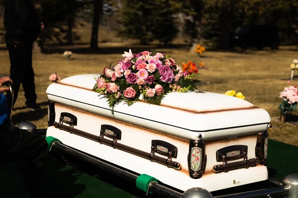 An elegant white casket adorned with a beautiful spray of pink and purple flowers resting peacefully in a serene Southern Alberta cemetery.